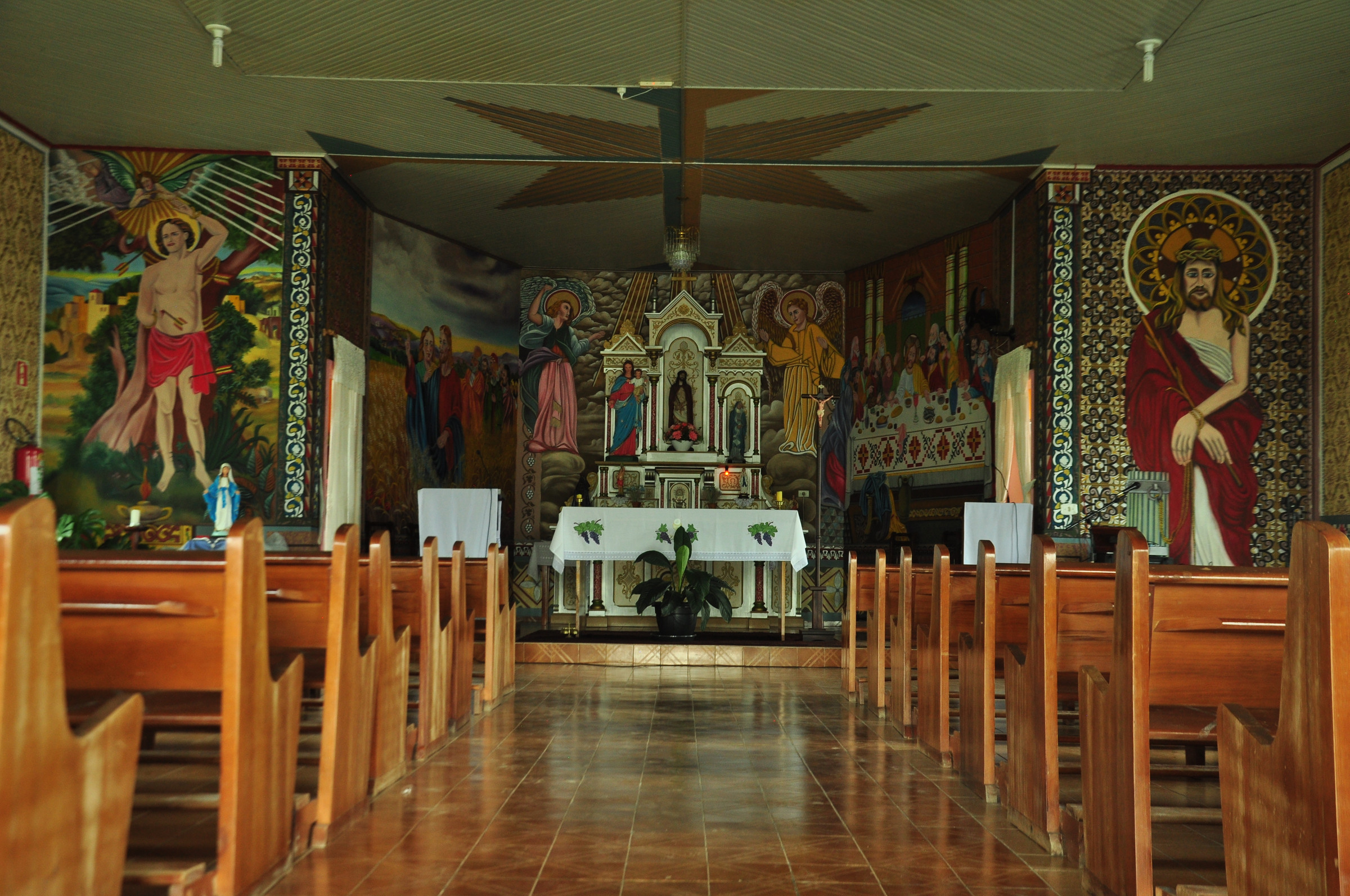 Bancos de madeira conduzem a um altar cercado por pinturas e imagens religiosas.